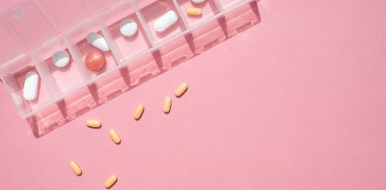 A clear pill container with different pills, on a pink background.
