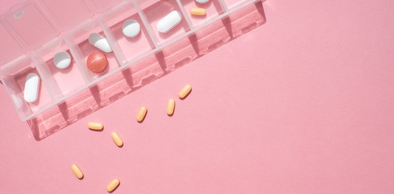 A clear pill container with different pills, on a pink background.