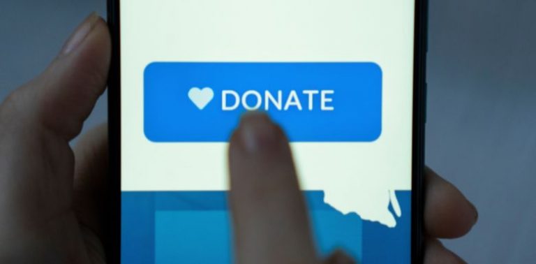 A finger tapping a "Donate" button on a cell phone screen.