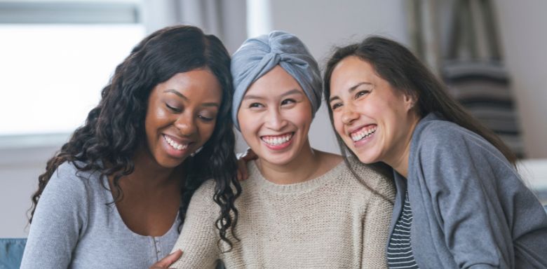 Three women sitting together with their arms around each other, smiling.