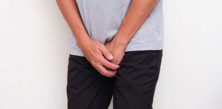 A man holding both of his hands over his groin.