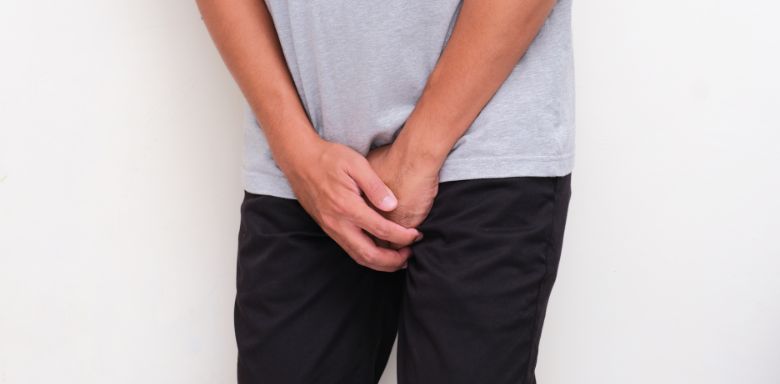 A man holding both of his hands over his groin.