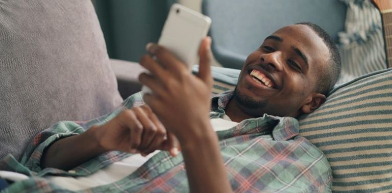 A man laying down, using a cell phone.