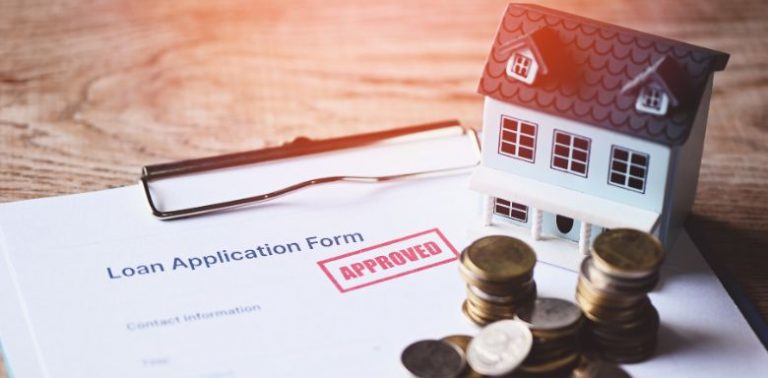 A model home and a pile of coins on top of paperwork that says "approved" in bold red lettering
