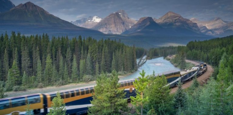 A passenger train traveling along a lake in the Canadian rocky mountains.