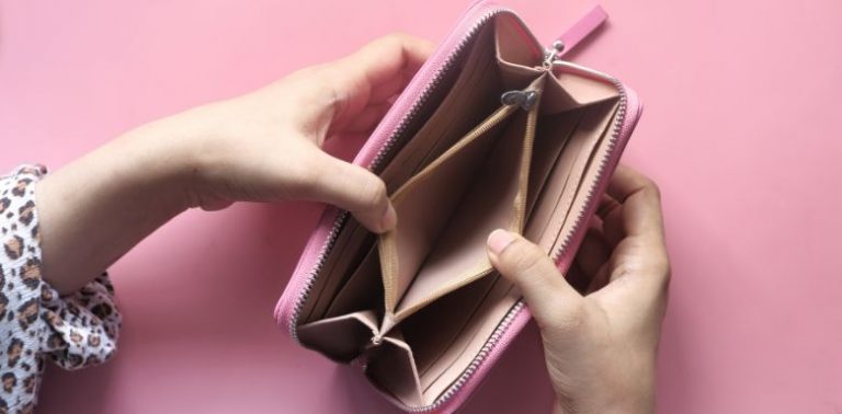 A woman holding an empty wallet open against a pink background.