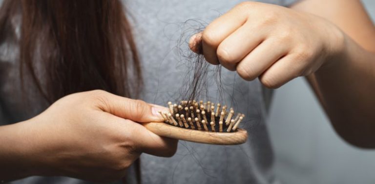 A woman pulling a handful of hair out of a brush.