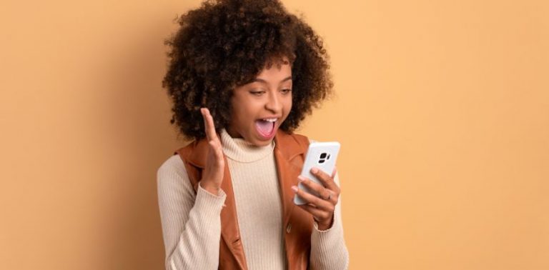A woman holding a cell phone and looking excited.