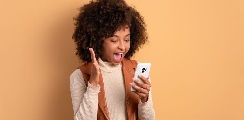 A woman holding a cell phone and looking excited.
