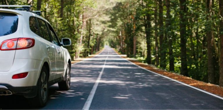 A white SUV on a road in a forested area.