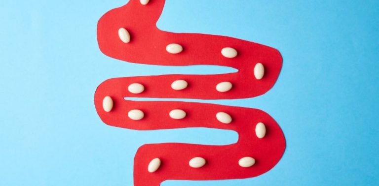 An illustration of white pills traveling down a red digestive tract on a blue background.