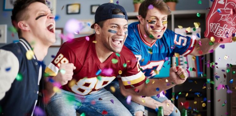 Three football fans, wearing jerseys and cheering together.