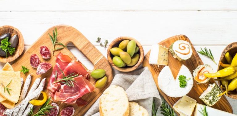 A charcuterie board with different processed meats, cheese, and some fruit.