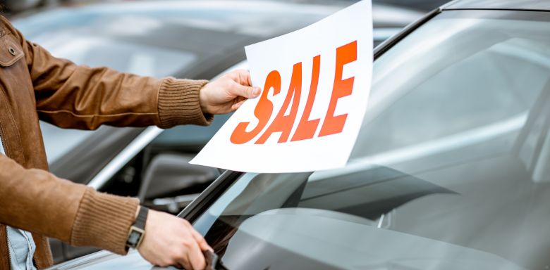 A person putting a large SALE sign on a car.